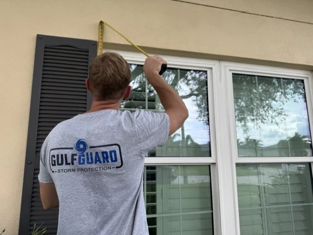 GulfGuard team member measuring the height of a double window opening for custom hurricane fabric protection.